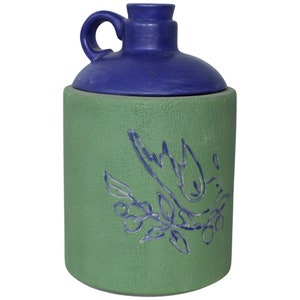 May include: A green ceramic jar with a blue lid and a blue bird design. The jar has a textured surface and a wide mouth.