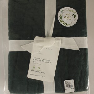 May include: A dark green Belgian flax linen hand-stitched sham, wrapped with a white ribbon and bow. The packaging includes a tag with product details and a sticker that says "Thank you". The sham measures 26 x 26 inches.