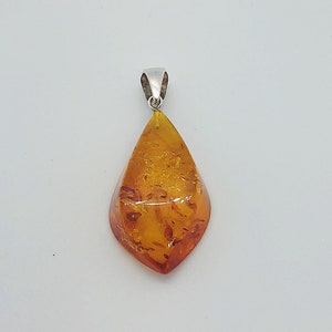 May include: A teardrop-shaped amber pendant with a silver bail. The amber is a deep orange color with inclusions.