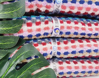 May include: A stack of colorful, patterned towels. The towels feature a repeating square design in shades of red, blue, pink, and beige. Each towel is wrapped with a white ribbon that has text and an eye symbol.