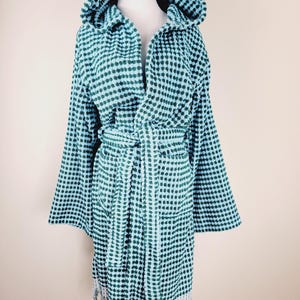 May include: A teal and white patterned hooded bathrobe with a matching belt. The robe has a textured dot pattern and a fringe detail at the hem. The robe is displayed on a mannequin.