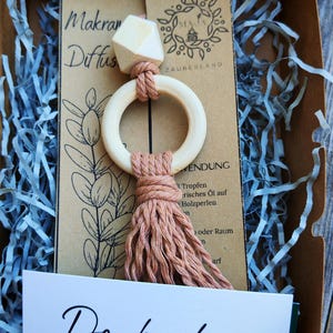Könnte beinhalten: Ein hölzerner Aromatherapie-Diffusor mit geometrischem Aufsatz, einem kreisförmigen Holzring und einer Quaste. Der Diffusor ist in einem Karton mit blauem Papier verpackt und enthält eine Karte mit "Dankeschön".
