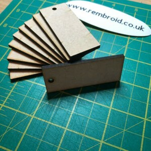 May include: A collection of rectangular, unfinished wooden tags, each with a small hole for hanging. The tags are arranged on a green cutting mat. A white oval with the text "www.rembroid.co.uk" is also visible.