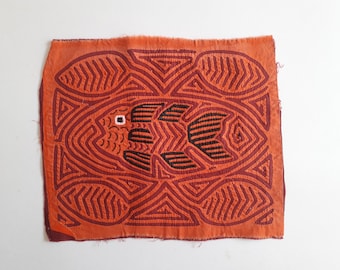 May include: A red and black textile with a geometric pattern of a fish in the center. The fish is surrounded by a series of concentric circles and triangles.
