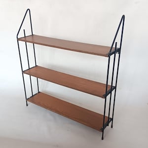 Könnte beinhalten: Ein dreistufiges Wandregal im Mid-Century-Modern-Design. Die Regale sind aus hellbraunem Holz gefertigt und werden von einem schwarzen Metallrahmen getragen. Der Rahmen hat ein einzigartiges, abgewinkeltes Design.