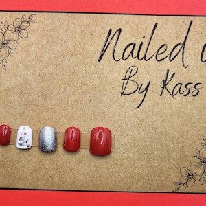 May include: A close-up of six red and silver nail art designs. The designs include a Christmas tree, a solid red, and a silver glitter design. The text "Nailed it By Kass" is written on a brown background.