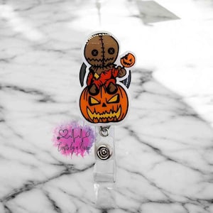 May include: A Halloween-themed retractable badge holder with a cartoon image of a stitched-up doll holding a candy corn on top of a jack-o'-lantern.