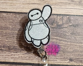 May include: A silver glitter Baymax character badge reel with a clear plastic retractable badge holder. The reel has a silver metal clip and a silver metal ring.