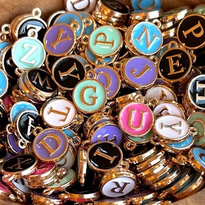 May include: A pile of gold-colored metal charms with different colored enamel letters on them. The letters are A, B, C, D, E, F, G, H, I, J, K, L, M, N, O, P, Q, R, S, T, U, V, W, X, Y, and Z.