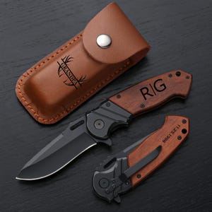 May include: A personalized pocket knife with a brown wooden handle and a black blade. The handle is engraved with the initials "R/G" and the words "Grandpa" and "11.23.1966". The knife comes with a brown leather sheath.