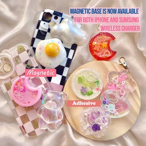 May include: An assortment of decorative phone accessories, including a clear bear, a fried egg, and a cloud. The accessories are in various colors and shapes, with the text "Magnetic Base is Now Available" and "Wireless Charger".