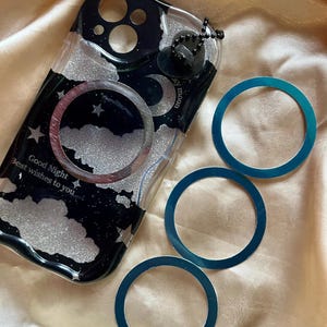 May include: A black and white phone case with a glitter finish and a moon and stars design. The case has a clear back and a black border. The text "Good Night best wishes to you" is printed on the case. Three blue rings are also included in the image.