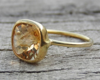 May include: A gold ring with a large, square-shaped, light brown gemstone.