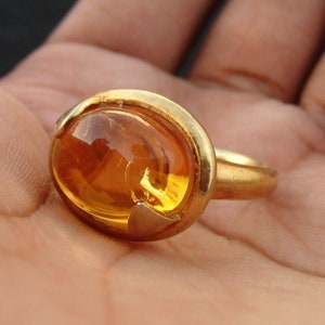 May include: A gold ring featuring a large, oval-shaped amber gemstone.