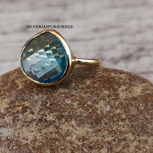 May include: A gold ring with a large, teardrop-shaped blue gemstone. The ring is set on a rough, brown rock.