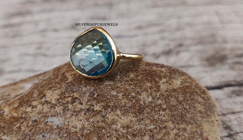 May include: A gold ring with a large, teardrop-shaped blue gemstone. The ring is set on a rough, brown rock.
