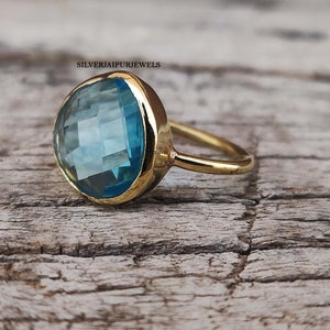 May include: A gold ring with a large, round, light blue gemstone. The gemstone has a faceted cut and is set in a bezel setting.