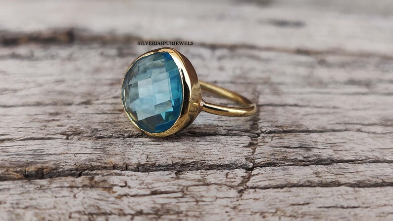 May include: A gold ring with a large, round, light blue gemstone. The gemstone has a faceted cut and is set in a bezel setting.