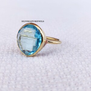 May include: A gold ring featuring a large, light blue gemstone with a faceted cut. The ring has a simple band and a bezel setting. The text "SILVERJAIPURJEWELS" is visible in the upper left corner.