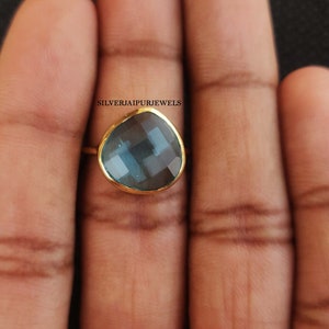May include: A gold ring with a blue gemstone. The gemstone is faceted and has a teardrop shape.