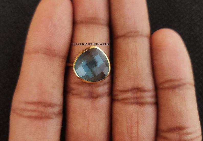 May include: A gold ring with a blue gemstone. The gemstone is faceted and has a teardrop shape.