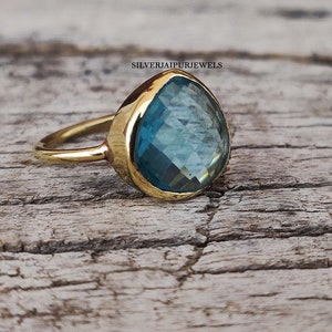 May include: A gold ring with a large, teardrop-shaped blue gemstone. The ring is set on a wooden surface.