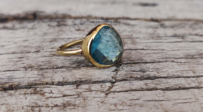 May include: A gold ring with a large, teardrop-shaped blue gemstone. The ring is set on a wooden surface.