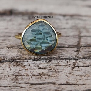 May include: A gold ring with a teardrop-shaped blue gemstone. The gemstone has a faceted cut and is set in a gold band.