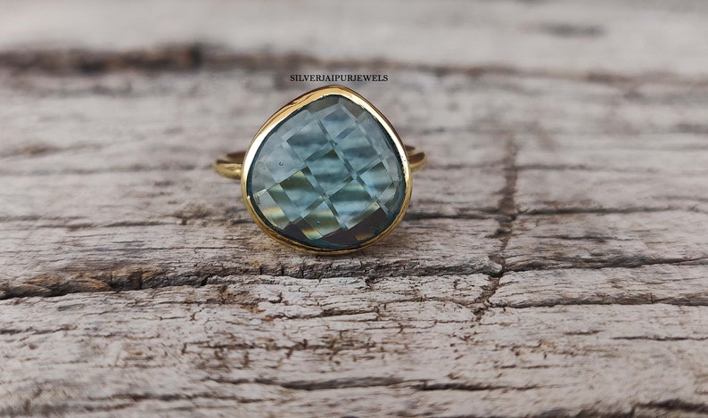 May include: A gold ring with a teardrop-shaped blue gemstone. The gemstone has a faceted cut and is set in a gold band.