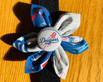 May include: A blue and white fabric flower with a black velcro strap. The flower has a button in the center with the word "Dodgers" in white text.