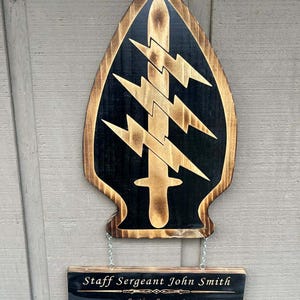 May include: Wooden plaque featuring a black and brown design of a Special Forces symbol with a sword and lightning bolts. Below, a smaller plaque reads "Staff Sergeant John Smith, Section Sergeant, January 2023-January 2025."