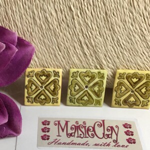May include: Three ceramic tiles with a yellow background and a brown clover design. The tiles are square and have a glossy finish. The text "MaisieClay Handmade, with love" is visible in the bottom right corner of the image.