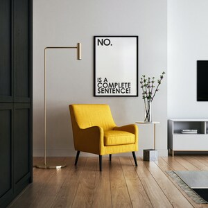 Può includere: Un moderno soggiorno con una poltrona gialla, una lampada da terra dorata e una stampa incorniciata con la scritta "NO. IS A COMPLETE SENTENCE!". La stanza ha pavimenti in legno e un'estetica minimalista.