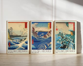 May include: Three framed art prints featuring Japanese woodblock prints by Utagawa Hiroshige. Each print depicts ocean waves in shades of blue, with text in Japanese and English. The frames are a light beige color.