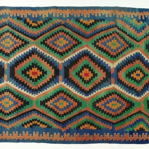 May include: A colorful rug with a geometric pattern in shades of blue, green, orange, and black. The rug has a fringe border.
