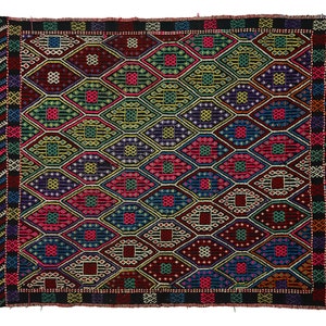 May include: A colourful rug with a geometric pattern of diamonds and squares in shades of red, blue, green, yellow, and black. The rug has a black fringed border.