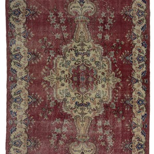 May include: A vintage rug with a faded red background and a cream-colored floral pattern. The rug has a central medallion with intricate details and a border with a repeating design.