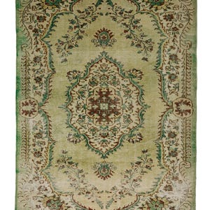 Puede incluir: Una alfombra vintage con un borde verde y un centro de color crema. La alfombra presenta un patrón floral con intrincados detalles en tonos verdes, marrones y crema.