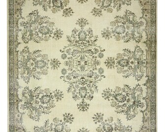May include: A vintage cream-colored rug with a floral pattern in shades of brown and green. The rug has a border with a repeating pattern.