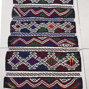 May include: A colorful woven rug with geometric patterns in shades of red, blue, green, white, and black. The rug has a fringe border.