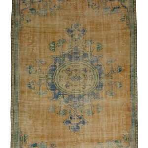 Könnte beinhalten: Rechteckiger, abgenutzter Teppich mit einem zentralen Medaillon-Design. Der Teppich hat ein warmes, goldgelbes Feld mit verblassten blauen und türkisfarbenen Blumenmustern. Ein türkisfarbener Rand umrahmt den Teppich und verleiht ihm eine Vintage-Ästhetik.