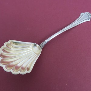 May include: A silver sugar spoon with a shell-shaped bowl. The spoon has a decorative handle and is in good condition.