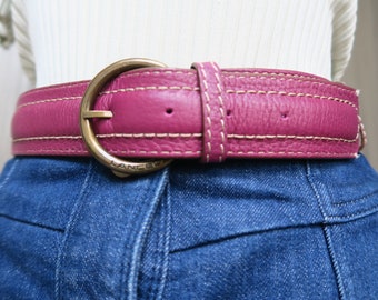 May include: A pink leather belt with a gold buckle and stitching. The buckle has the word "LANCO" engraved on it.
