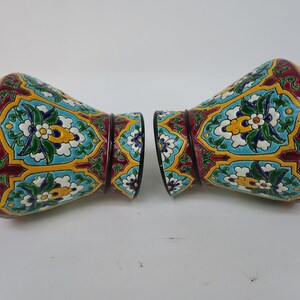 May include: A pair of decorative ceramic vases with a colorful floral pattern. The vases are a deep red, yellow, blue, green, and white. The vases have a black base.