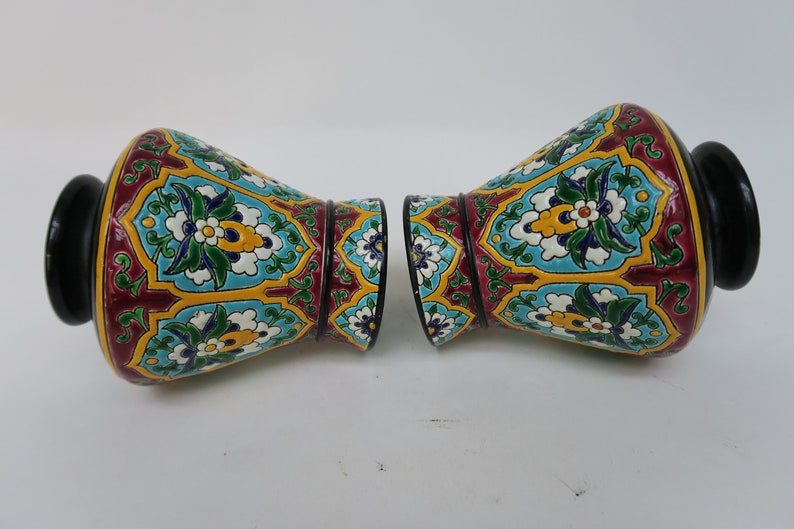 May include: A pair of decorative ceramic vases with a colorful floral pattern. The vases are a deep red, yellow, blue, green, and white. The vases have a black base.