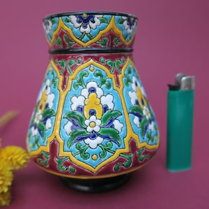 May include: A small, colorful ceramic vase with a geometric and floral design. The vase is decorated with blue, green, yellow, white, and red paint.