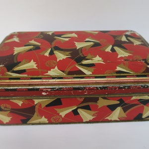 May include: A vintage tin box with a red, black and gold geometric pattern featuring stylised flowers. The box has a worn, distressed look.
