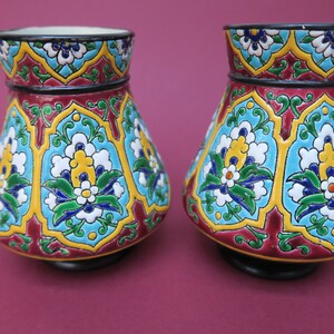 May include: Two ceramic vases with a colorful floral pattern. The vases are decorated with blue, green, yellow, white, and red flowers on a blue background. The vases have a black base.