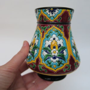 May include: A small, decorative vase with a bulbous body and a flared rim. The vase is decorated with a colorful floral pattern in shades of blue, green, yellow, and white on a burgundy background.