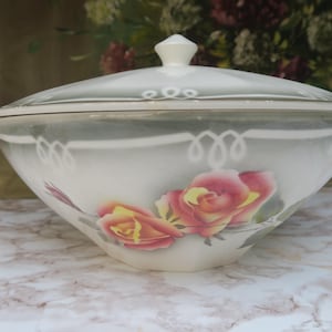 Peut inclure: Soupière en porcelaine blanche avec couvercle, ornée d'un motif floral de roses roses et jaunes. La soupière est bordée d'une frise décorative sur fond gris.